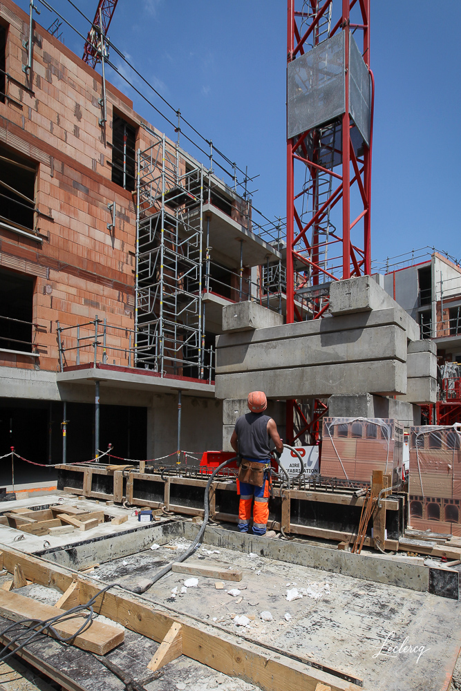 Ouvrier du bâtiment travaillant au pied d'une grue sur un chantier de construction d'immeuble en briques, photographié par Ludovic Leclercq.