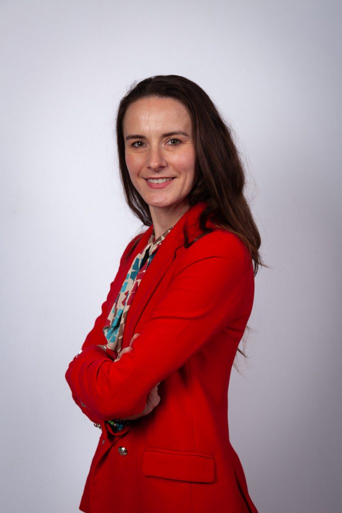 Portrait professionnelle d'une femme en veste rouge sur fond blanc.